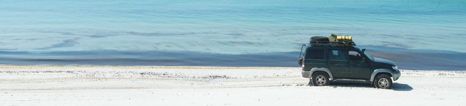 透明度の高い青い海の前に停車した荷物を積んだ四輪駆動車