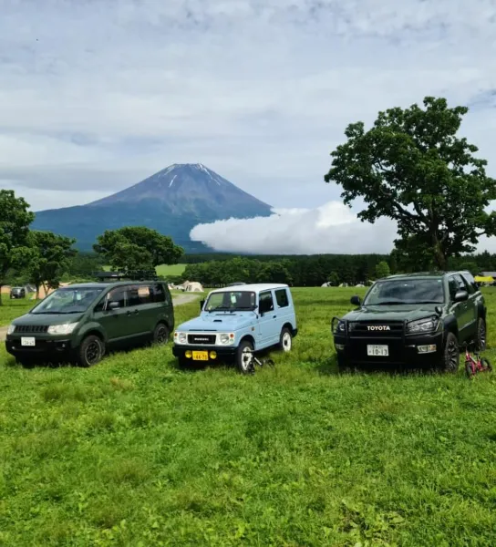緑の草原に並ぶ3台の車と、背景にそびえる富士山の風景