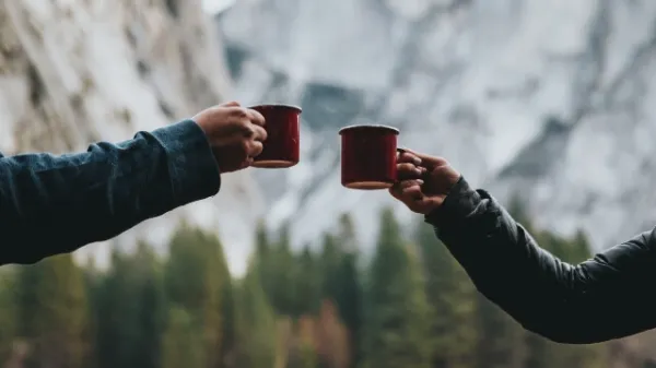 山の風景を背景に、赤いマグカップで乾杯している2人の手元