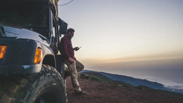 ジープのような車にもたれかかり、スマートフォンを見ている男性