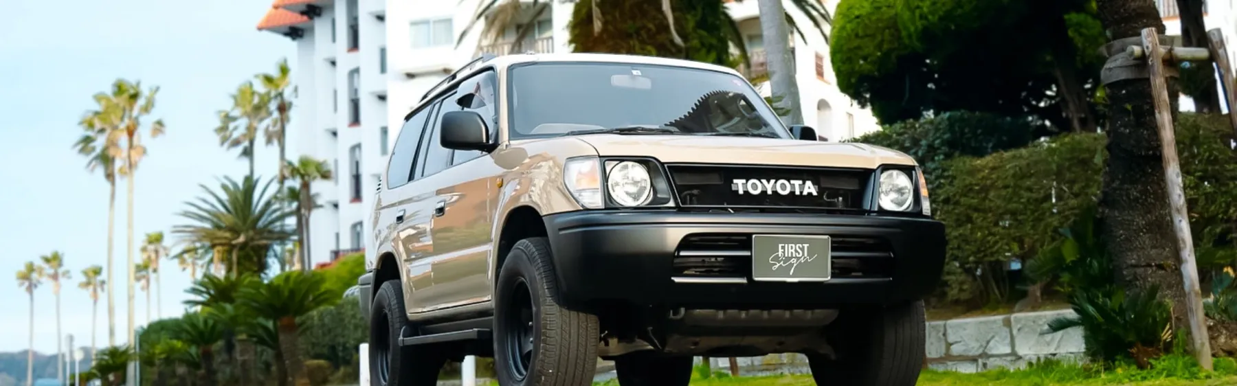 南国風の街並みを背景に、ベージュと黒のツートンカラーSUVが停車している様子