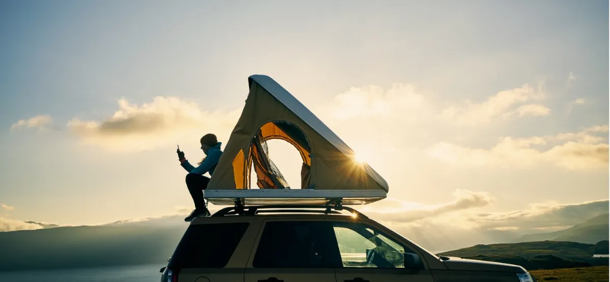 車の屋根に設置されたテントに座る人物と、夕日が差し込む風景