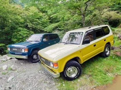 渓流近くの林道に並ぶ黄色と緑のクラシックSUVのツーショット