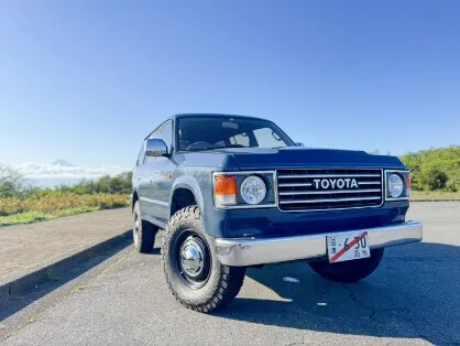 青空の下、舗装路に停車した青いトヨタSUVと遠景に見える富士山