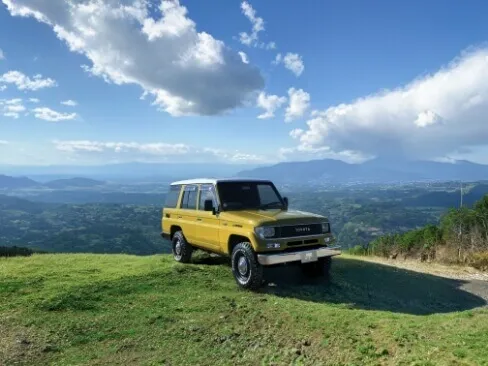 緑の丘の上に停車した黄色のトヨタSUVと広がる山々の風景