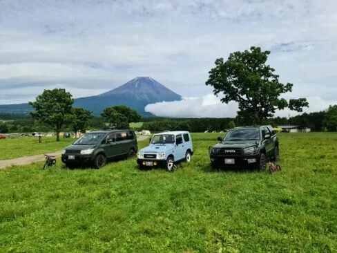 富士山を背景に並ぶ3台のSUVと緑の草原のキャンプ地