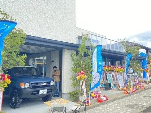 店舗の前に飾られた青いトヨタSUVと多数の開店祝いの花