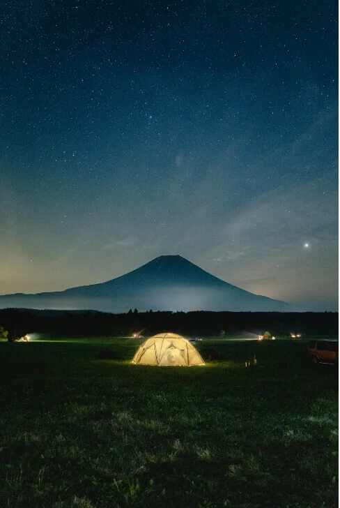富士山を背景に星空の下で光るキャンプテントの幻想的な風景