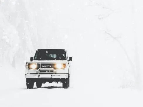 吹雪の中を走る白いトヨタSUVが前方からこちらに向かう