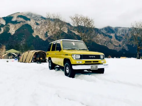 雪原を走る黄色のトヨタSUVと奥に広がる雪山の風景
