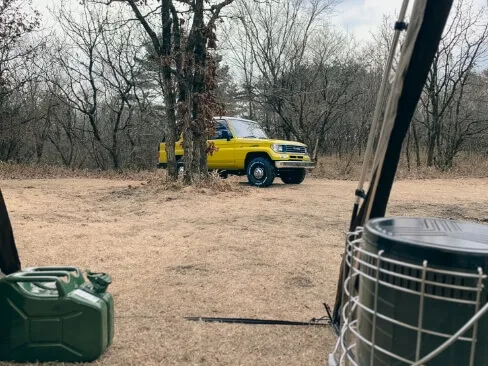 キャンプ道具越しに見える黄色の四駆と自然の風景
