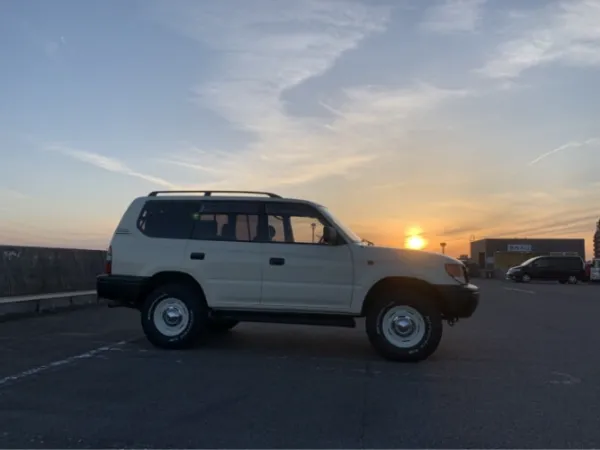 夕日が沈む空を背景に駐車場に停められた白いSUVの横向きの写真