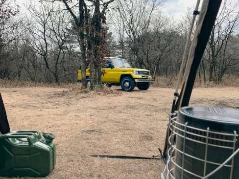 枯れた草地に停まる黄色いSUVをテント内から撮影したアウトドア風景